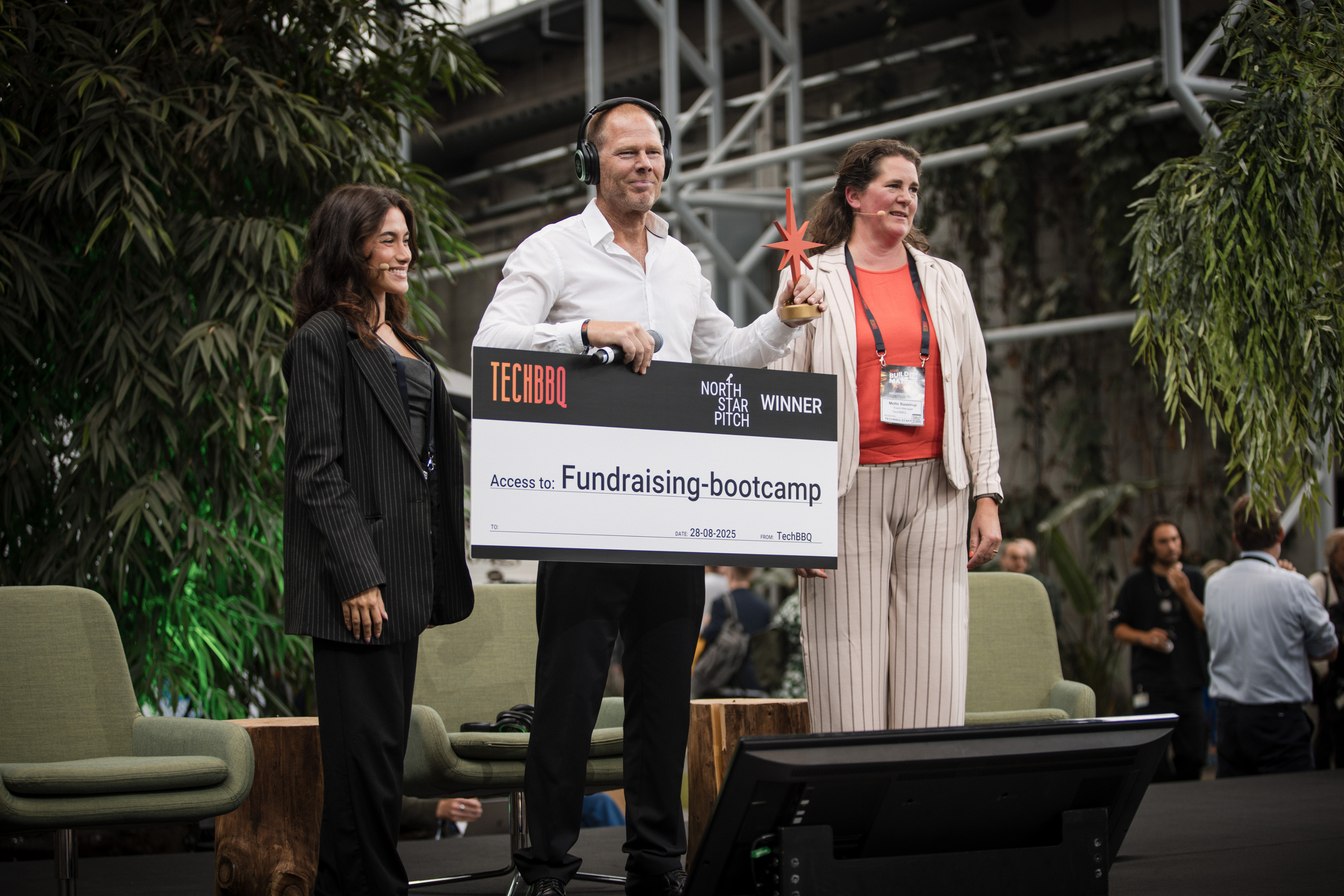 North Star Pitch winner on stage holding a Fundraising Bootcamp access prize